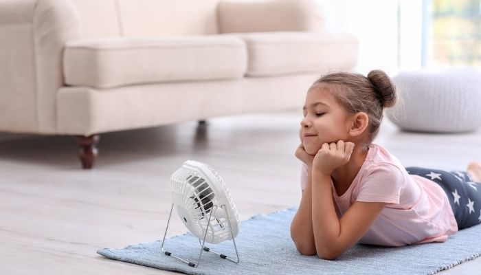 Little girl in front of a small fan indoors