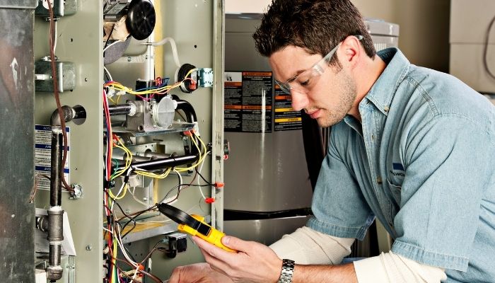 HVAC technician using a multimeter to test furnace wiring while checking a burning smell from heater